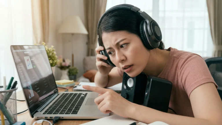 หญิงสาวสวมหูฟังทำหน้าสงสัยและชี้ไปที่หน้าจอโน๊ตบุ๊คเมื่อเสียงหายไป